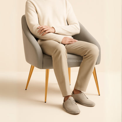 Person sitting on a modern chair wearing a beige sweater, pants, and shoes against a plain background.
