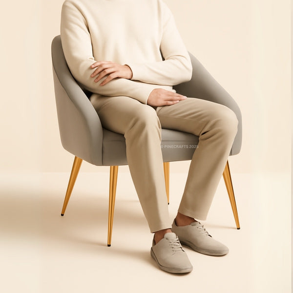 Person sitting on a modern chair wearing a beige sweater, pants, and shoes against a plain background.