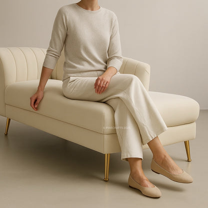 Person sitting on a beige armchair wearing a beige sweater, white pants, and beige shoes.