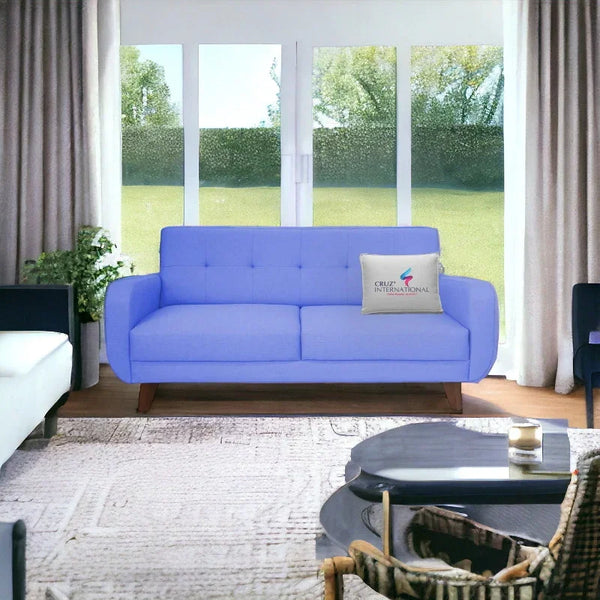 Blue modern sofa with CRUZ INTERNATIONAL pillow in bright living room, large windows, wooden legs