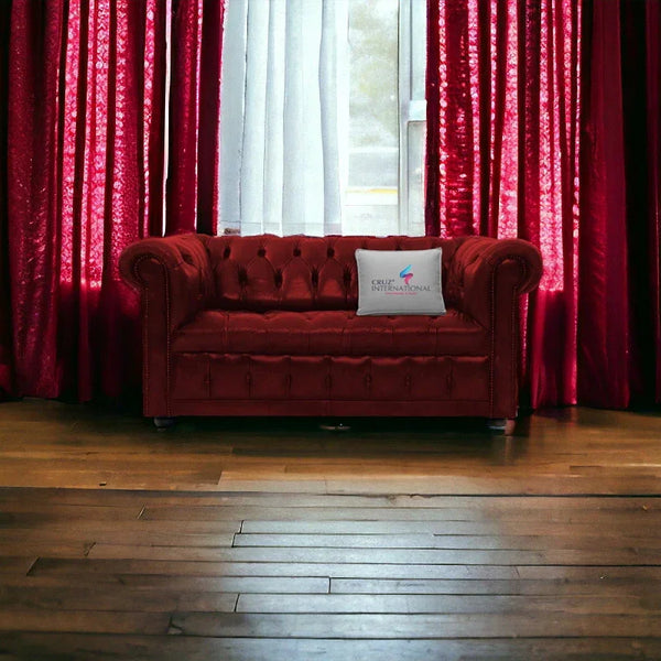 Maroon tufted sofa with CRUZ INTERNATIONAL cushion, set against red curtains and wooden floor.