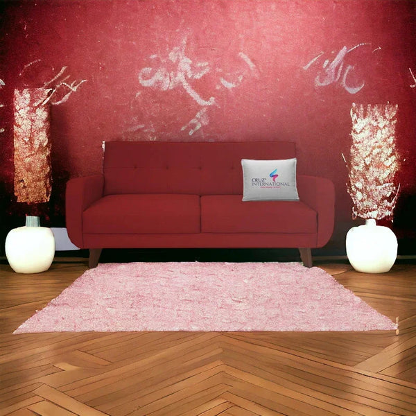 Modern maroon sofa with CRUZ INTERNATIONAL pillow, pink rug, and contemporary décor in a stylish living room.