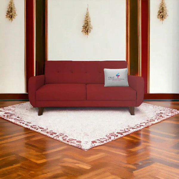 Maroon sofa on white rug with CRUZ INTERNATIONAL pillow, modern living room setting