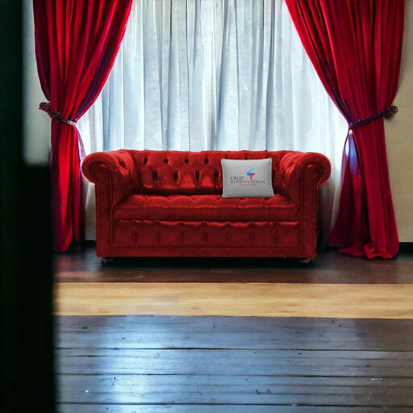 Red chesterfield sofa with CRUZ INTERNATIONAL pillow, red curtains, and wooden floor